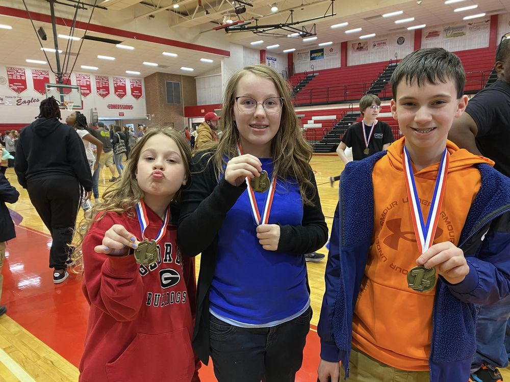 Three odyssey of the mind students hold up their medals