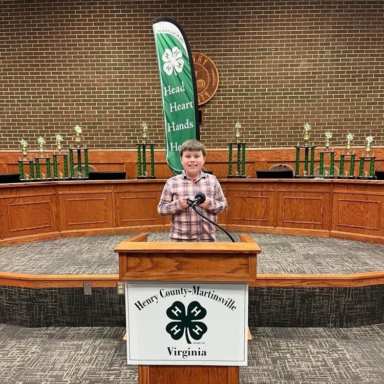 PHES student Archer Deatherage stands at 4H podium with trophies on a desk in the background