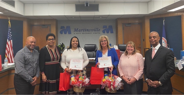 Members of the Martinsville City School Board and the MCPS superintendent stand with the school board clerk and assistant clerk. the clerks are holding gift baskets and certificates  