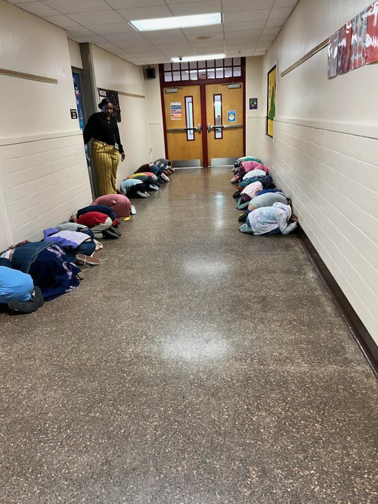 Students kneel and cover their heads in the hallway