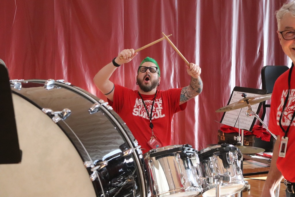 MMS teacher Greg Hackenberg holds drumsticks in the air as he sits behind a silver drum kit