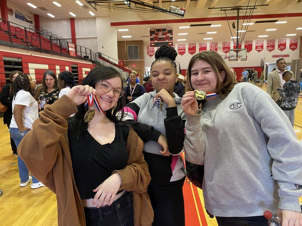 Middle school Odyssey of the Mind team members hold up their first place medals