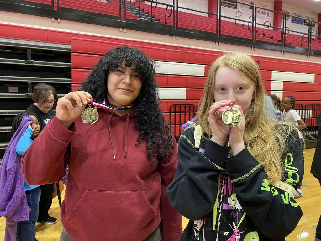 Middle school Odyssey of the Mind team members hold up their first place medals
