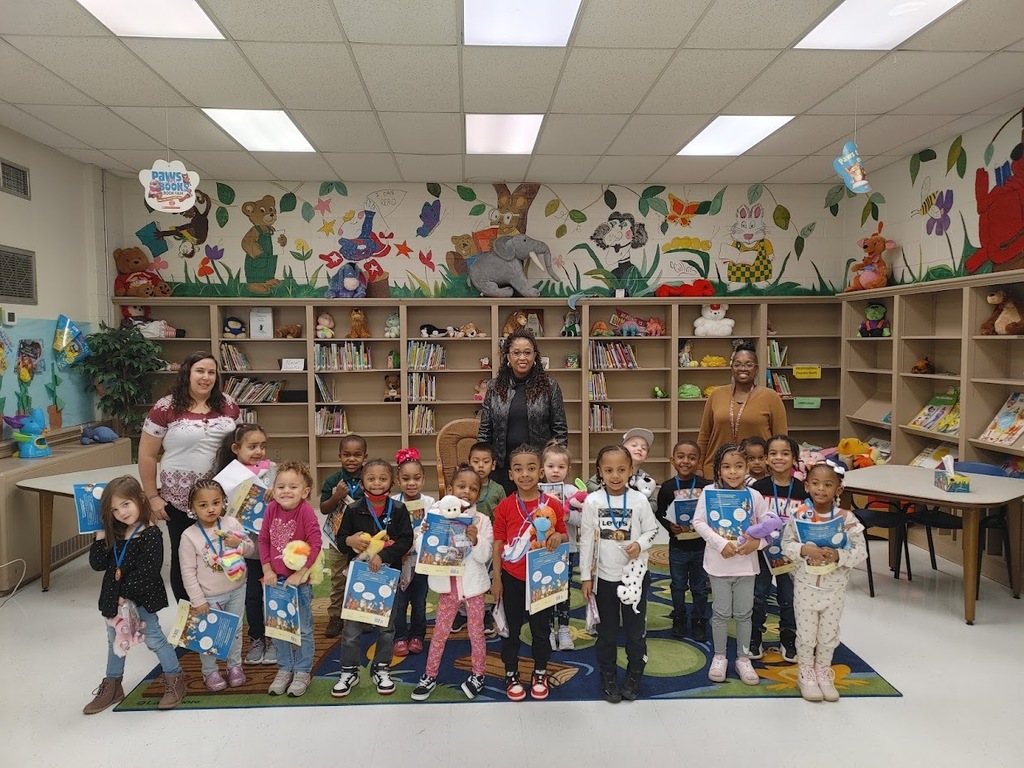 A group of Clearview students hold stuffed animals and one book each. Behind them are two teachers and the director of the preschool.