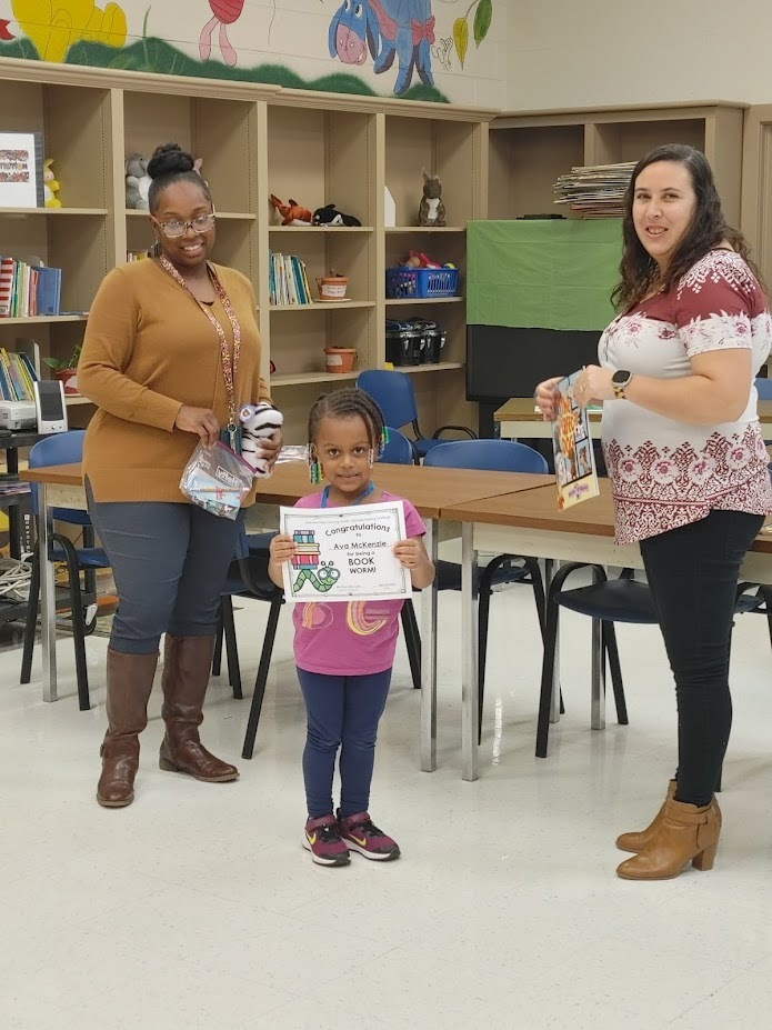 A Clearview student holds up a reading certificate as two teachers look on