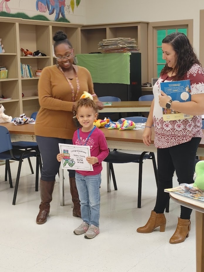 A Clearview student smiles as she holds up a reading certificate as two smiling teachers look on