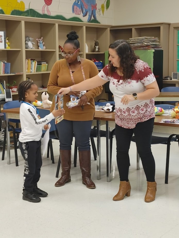 Two teachers hand a Clearview student a book and a prize