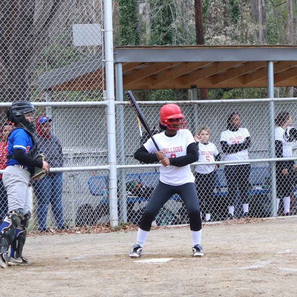 A middle school softball player stands with a bat at the ready at home plate