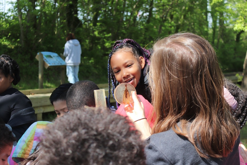 An AHES student smiles at an example of a macro-invertebrate being held up by a DRBA instructor