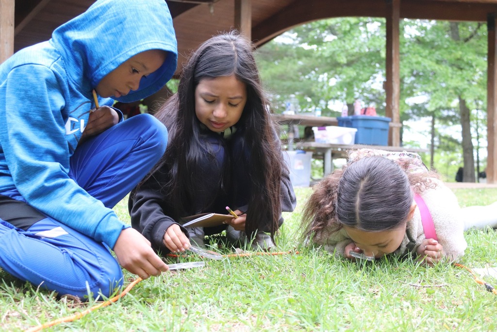 AHES students examine the ground with magnifying glasses